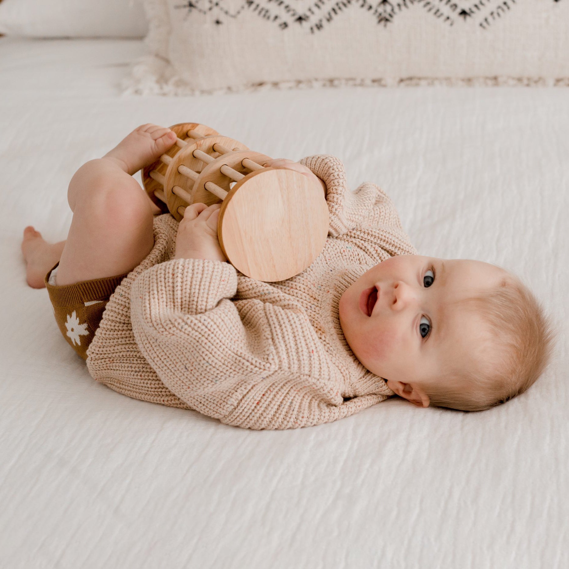 baby sitting on bed playing with qtoys rainmaker wooden toy