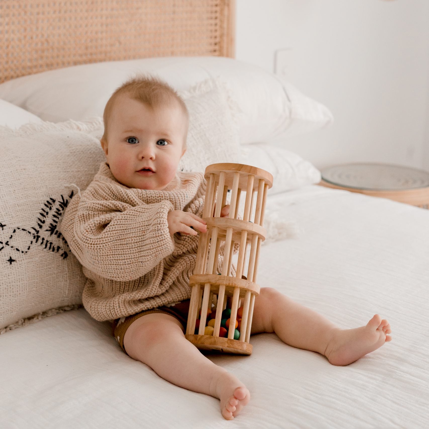 baby sitting on bed playing with qtoys rainmaker wooden toy